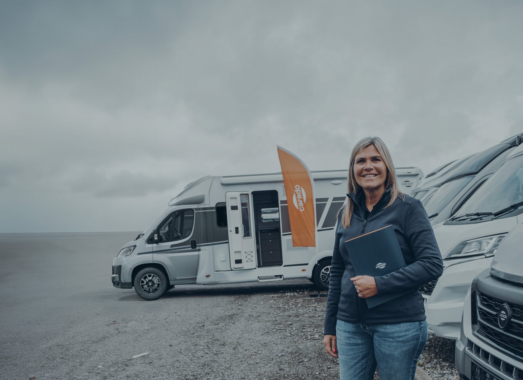 Woman with a portfolio in front of Carado motorhomes at a pitch by the water